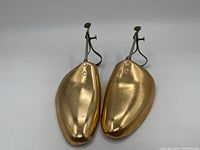 Pair of gold-colored polished metal shoe forms top view showing size and shape with adjustment screws and straps.