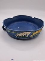 Front side view of the large blue Roseville ceramic bowl with raised yellow and white floral decorations and green leaves.