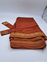 Folded rust orange sari with gold embroidered borders laid flat