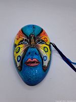 Front view of the blue Venetian style ceramic mask with painted butterfly design covering nose and cheeks.
