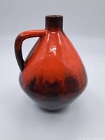 Front and side views of the vintage Blue Mountain pottery jug/vase showing rounded body and handle with reddish-orange to dark brown glaze.