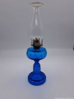 Full view of the vintage cobalt blue glass oil lamp showing the clear glass chimney, metal burner, and textured blue glass base and reservoir.