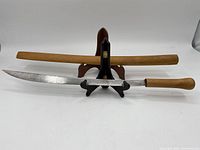 Full view of the katana sword laid in front of a wooden sheath on a display stand.
