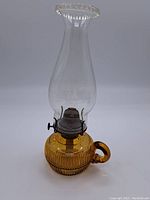 Full view of vintage oil lamp showing amber ribbed glass base with handle and clear glass chimney.