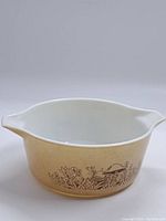Front angled view showing beige casserole dish with white interior, two pouring spouts and brown mushroom and foliage pattern.