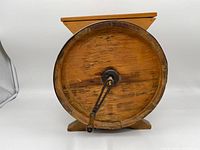 Full bottom view of wooden churn showing circular lid, metal crank mount, wood grain, and metal rim band.