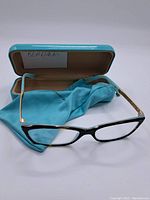 Two pairs of women's reading glasses displayed with teal hard case and matching cleaning cloth on a white background.