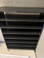 Front view of one black shelving unit showing 8 shelves and the flat top shelf, painted black, placed on a tiled floor.