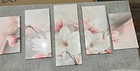 Five canvas panels arranged next to each other on a gray surface, showing a coordinated pink and white floral design.