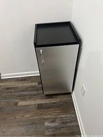 Front view of closed silver metal door with handle, black frame cabinet on wheels.