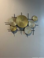 Front view of metal wall decor showing seven circular textured plates in gold and silver mounted on black iron rectangular frame