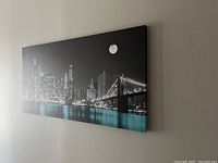 Angle view of stretched and framed New York City night skyline canvas wall art hanging on beige wall.