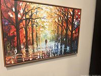 Full view of framed painting showing colorful autumn trees and pathway with two human figures.