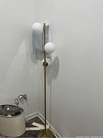 Full view of the floor lamp showing three white spherical glass globes attached to a brass stand with circular base.