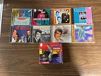 Top-down view of 10 music CDs featuring 1950s and 1960s artists and groups, arranged on a wooden surface.