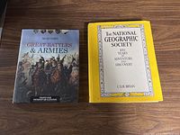 Two hardcover tabletop books side by side on a wooden surface: 'The National Geographic Society - 100 Years of Adventure and Discovery' with a yellow cover and 'Great Battles & Armies' with an illustrated cover of cavalry warriors.