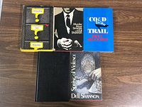 Five hardcover Dell Shannon books arranged on wood surface, with four having slipcovers and one without.