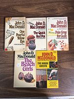 Top view of the five John D. MacDonald paperback books with visible titles and cover artwork.