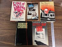 Five hardcover books by Lesley Egan with dust jackets on wooden surface. Titles shown include The Wine of Violence, Motive in Shadow, The Miser, Scenes of Crime, Little Boy Lost.