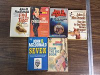 Front view of six John D. MacDonald paperback books arranged in two rows on a wooden surface.