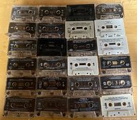 Twenty-two 1990s music audio cassettes arranged in a 5x5 grid with some gaps, showing different labels and colors mainly black and clear plastic.