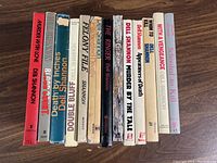 Photo showing the spines of all 13 hardcover books by Dell Shannon arranged side by side, titles visible.