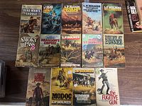 Photo showing 14 paperback Western books by L.P. Holmes, laying flat in rows on a wooden surface.