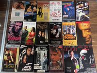 Top-down photo of 16 VHS movies laid out on a wooden surface, showing front covers and some spines, varied genres and titles visible.