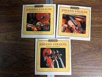 Front view of three Johann Strauss classical music CDs with yellow covers and string instrument images.