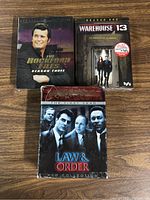 Front view of three DVD box sets: The Rockford Files Season 3, Warehouse 13 Season 1, and Law & Order The First Year with clear product branding and imagery.