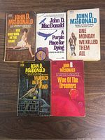 Front covers of the five John D. MacDonald paperback books laid out flat on a wooden surface.