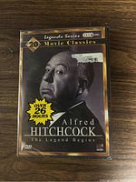 Front of sealed Alfred Hitchcock DVD set packaging with monochrome image of Hitchcock and text highlighting over 26 hours of content.