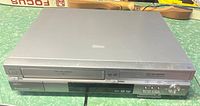 Front view of Panasonic VHS/DVD recorder unit showing VHS tape slot, DVD tray, and control buttons.