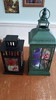 Front view of green and black decorative metal lanterns on table near wall.
