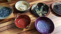 Six pieces of local pottery including plates and bowls in various earthy tones and glazes laid out on a hardwood floor.