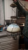 Full view of the chandelier held up showing metal frame, glass shade, and hanging crystals.