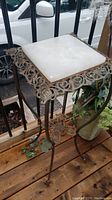 Full view of the antique iron table with marble top on wooden surface showing the overall design and condition.