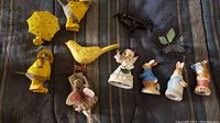 Overview photo of the collection showing 3 Enesco Peter Rabbit figurines, March angel, Fairy collection figurine, stained glass butterfly, metal crow, metal and wood yellow bird, and 3 resin birds in yellow jackets.