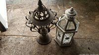 Two decorative metal lanterns, one brown with ornate cut metal designs, one white with glass panels
