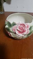 Close-up photo of the porcelain candle holder showing the pink rose and green leaves decorative detail on the creamy off-white base.