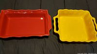 Both baking dishes side by side, red rectangular dish on left, yellow square dish with handles on right.