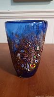 Front view of 8 inch blue glass vase with millefiori decoration on outside surface.