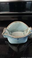 Front angle showing blue-green glazed ceramic dish with wing-like handles, ruffled rim, brown rim edging, and white interior.