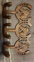 Three solid metal hooks with horse head and horseshoe design, showing overall view.
