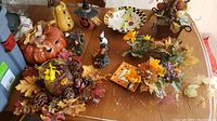 Fall themed decorative items arranged on a wooden table including artificial flowers, pumpkin decorations, and a fall plate.