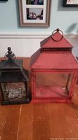 Front view of both metal lanterns on a wooden surface showing size and color difference.