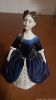 Front view of Royal Doulton Debbie porcelain figurine depicting a woman in a dark blue dress with white accents and patterned underlayer.