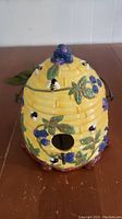 Front angle view of ceramic beehive birdhouse showing decorative bees, blackberries, and leaves