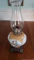 Full view of the Victorian oil lamp showing the top glass chimney, metal burner, hand painted milk glass body, and claw base
