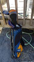 View of the full set of Wilson junior golf clubs including woods, iron, putter housed inside a blue and orange Wilson golf bag outdoors.